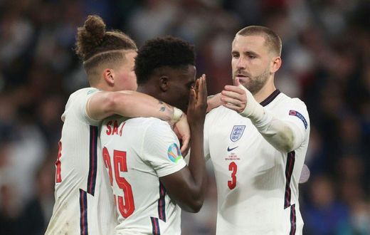 England's football team has united against raciism, Here midfielder Bukayo Saka (c) is consoled after failing to score in the penalty shootout of the Eur2020 final which England lost against Italy on Sunday