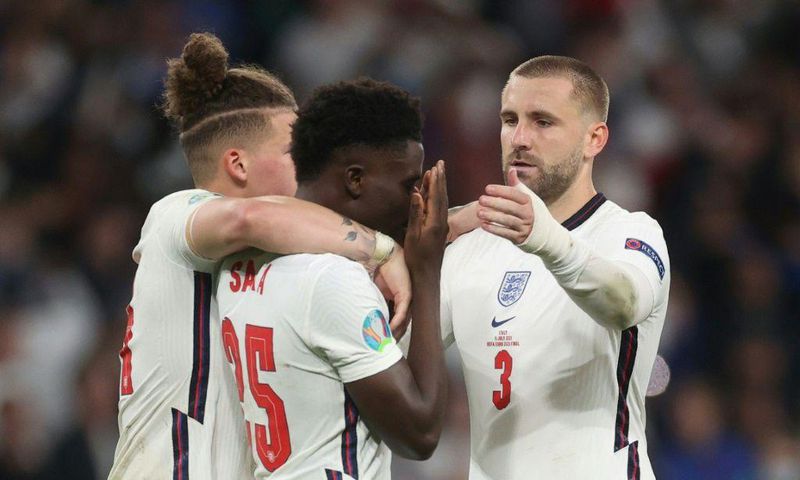 England's football team has united against raciism, Here midfielder Bukayo Saka (c) is consoled after failing to score in the penalty shootout of the Eur2020 final which England lost against Italy on Sunday