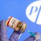 A coronavirus vaccine vial in front of the Pfizer logo.