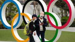 People in Japan wear masks due to the COVID-19 pandemic in front of Olympics rings.