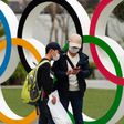 People in Japan wear masks due to the COVID-19 pandemic in front of Olympics rings.