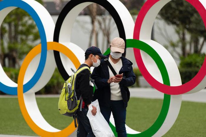 People in Japan wear masks due to the COVID-19 pandemic in front of Olympics rings.