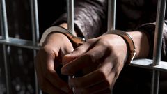 A prisoner behind bars with hands cuffed.Caspar Benson/Getty Images