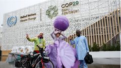 Chinese artist Kong Ning wearing a specially made "Purple Shells" art installation, poses with French climate activist David Ligouy of Peace Plus One and a visitor at the entrance of the venue during COP29. REUTERS/Murad Sezer.