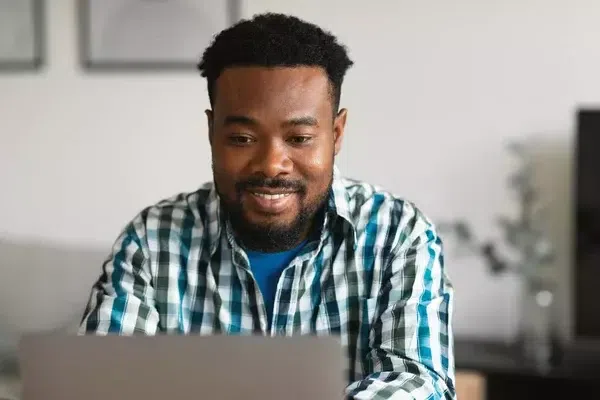 Cheerful Black man smiling at his laptop [Deposit Photos]