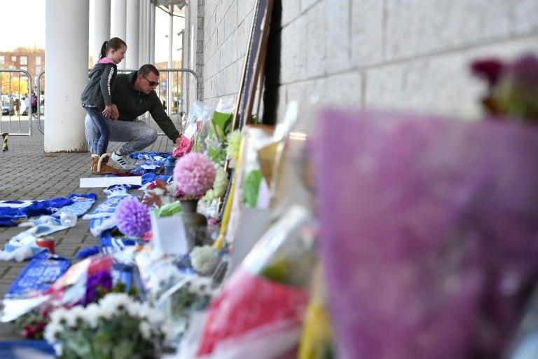A man and a girl add to flowers and football scarvess left as tributes outside Leicester City's King Power Stadium