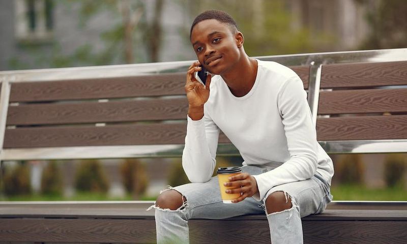 A young man using his phone while sitting on a park bench [Image: Gustavo Fring]