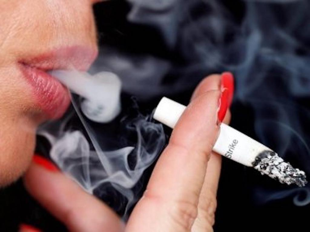 Smoke rises from a burning cigarette as a woman smokes on the street in Bordeaux