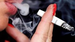 Smoke rises from a burning cigarette as a woman smokes on the street in Bordeaux
