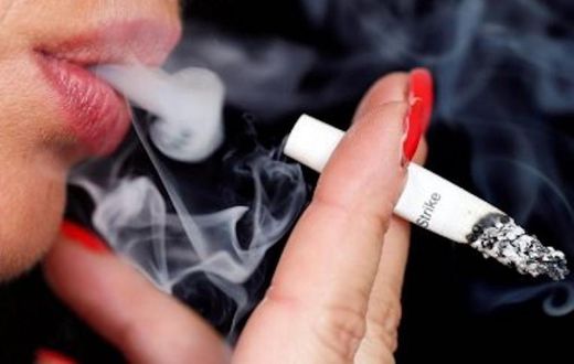 Smoke rises from a burning cigarette as a woman smokes on the street in Bordeaux