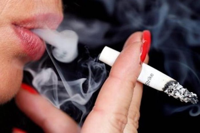Smoke rises from a burning cigarette as a woman smokes on the street in Bordeaux