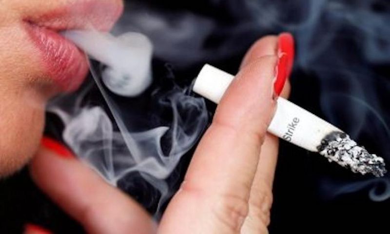 Smoke rises from a burning cigarette as a woman smokes on the street in Bordeaux