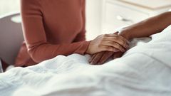 A woman holds a patients hand at a hospital.shapecharge/Getty Images