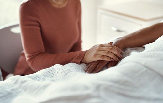 A woman holds a patients hand at a hospital.shapecharge/Getty Images