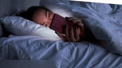 A woman lies in bed on her smartphone.Sergey Mironov/Getty Images