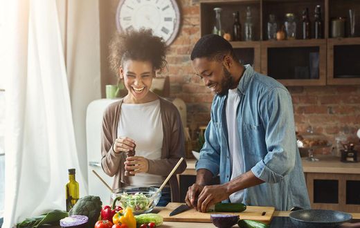 Laughing black couple preparing salad in kitchen