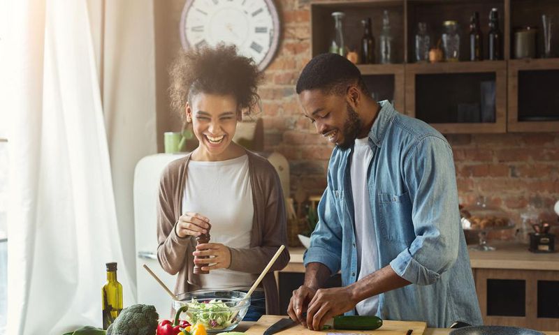 Laughing black couple preparing salad in kitchen