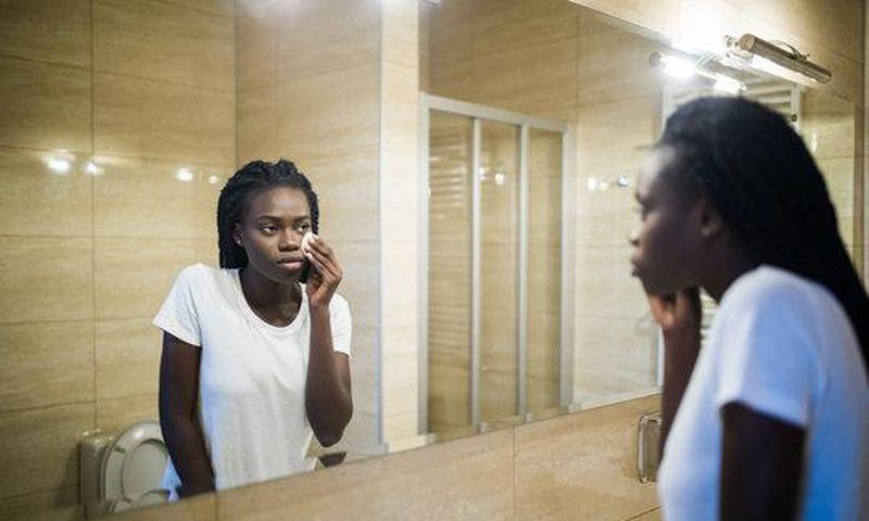 A Black woman looking in the mirror [Adobe Stock]