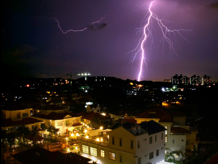 Lightning illuminates the horizon behind a Malaysian cityscape.
