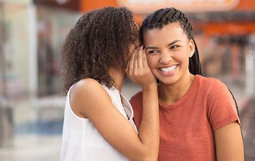 Black girl whispering secret to smiling girlfriend [Freepik]