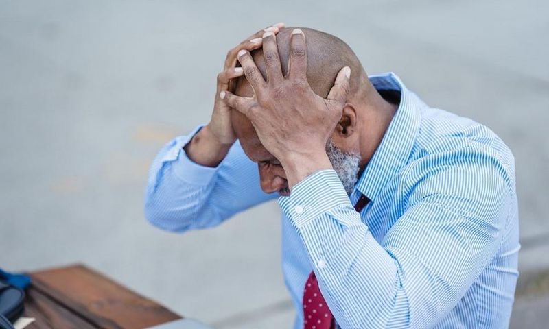 Concentrated black man grabbing head with hands sitting at table [Photo: Nicola Barts]