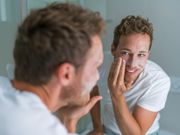 Man washing face with soap scrubbing exfoliation mask facial treatment looking in the mirror. Men taking care of skin, morning face wash routine for cleaning acne pimples.