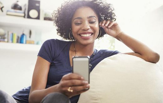 Smiling African American woman texting with cell phone on living room sofa