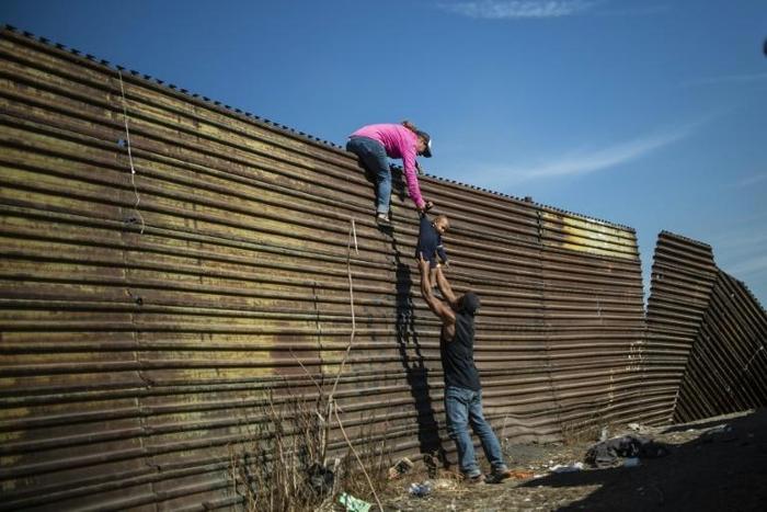 Central American migrants climb the border fence between Mexico and the United States in Tijuana, Mexico