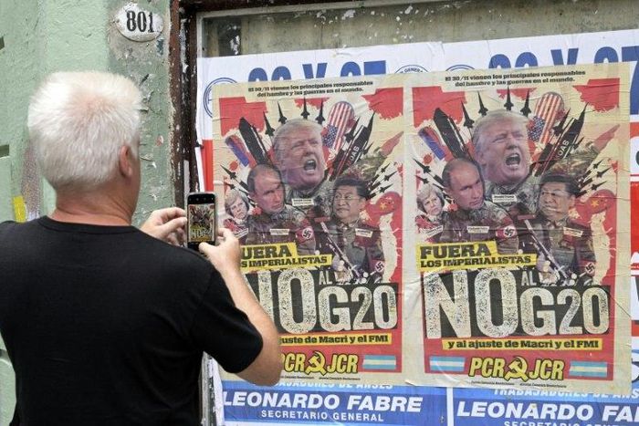 A passerby takes a picture of a poster protesting the G20 summit in Buenos Aires