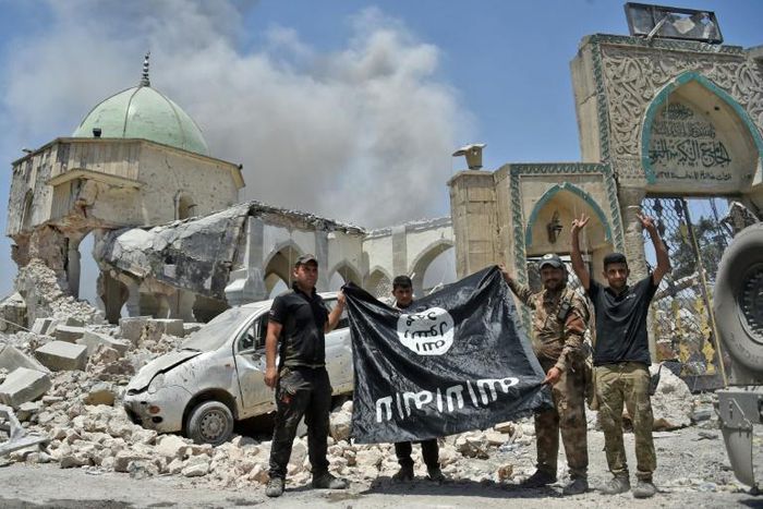 In this file photo taken on June 30, 2017 a member of Iraq's counter-terrorism squad flashes a victory sign as others hold upside-down an Islamic State group flag outside Al-Nuri Mosque in Mosul's Old City after IS was ousted from the area