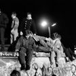 People from West Berlin climb over the Berlin Wall after its fall on November 9, 1989