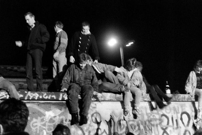 People from West Berlin climb over the Berlin Wall after its fall on November 9, 1989