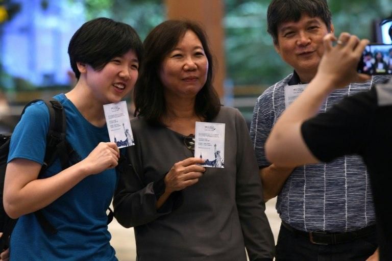 Singaporean William Chua (R) with family members, all passengers of flight SQ22, Singapore Airlines' inaugural non-stop flight to New York pose with souvenir cards after their their check-in at Changi International Airport in Singapore on October 11, 2...