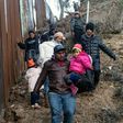 A group of Central American migrants walk alongside the Mexico-US border fence in Playas de Tijuana, Mexico