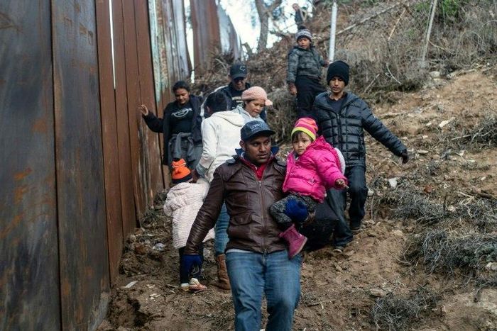 A group of Central American migrants walk alongside the Mexico-US border fence in Playas de Tijuana, Mexico
