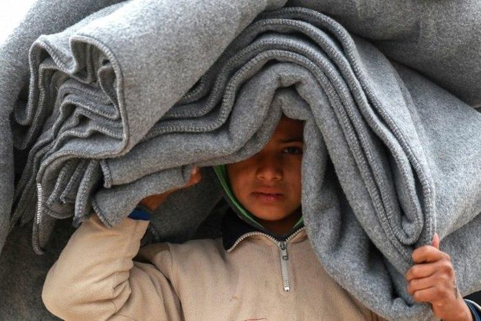 A Syrian displaced boy carries blankets over his head inside the Internallly Displaced Persons (IDP) camp of Al-Hol in northeast Syria