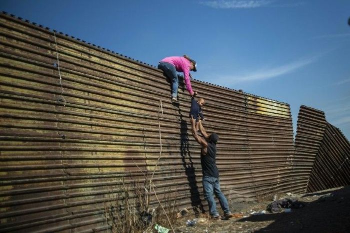 A group of Central American migrants climb the border fence between Mexico and the United States near El Chaparral border crossing in Tijuana -- the crisis is ongoing