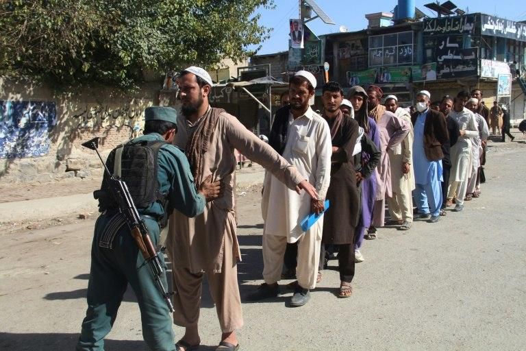 An Afghan policeman searches voters waiting to cast their vote during polls last month