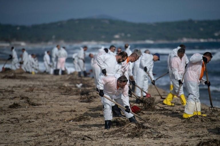 Workers clean up oily residues on Pampelonne beach in the Gulf of Saint-Tropez which leaked during a collision between two ships off Corsica on October 7