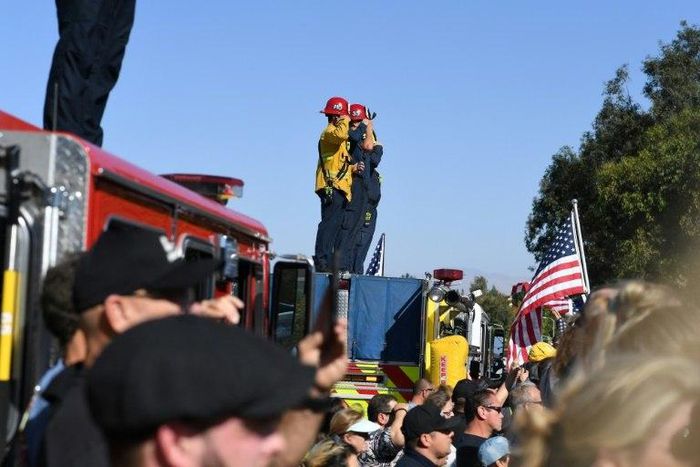 Firefighters salute as a motorcade passes by transporting the body of Sergeant Ron Helus, killed in a shooting at a country bar in Thousand Oaks, California
