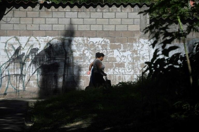 A woman briskly walks by a wall scrawled with gang graffiti in the Las Margaritas neighborhood of Soyapango, in San Salvador