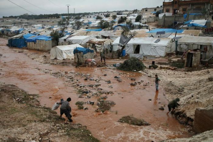 Displaced Syrians walk through a flooded camp near Qah in the northeastern Idlib province on December 27, 2018