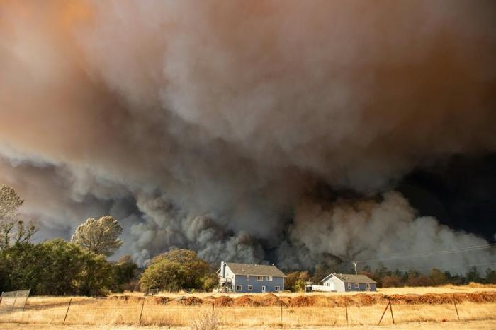 In this photo taken on November 8, 2018 a home is overshadowed by towering smoke plumes as the Camp fire races through town in Paradise, California