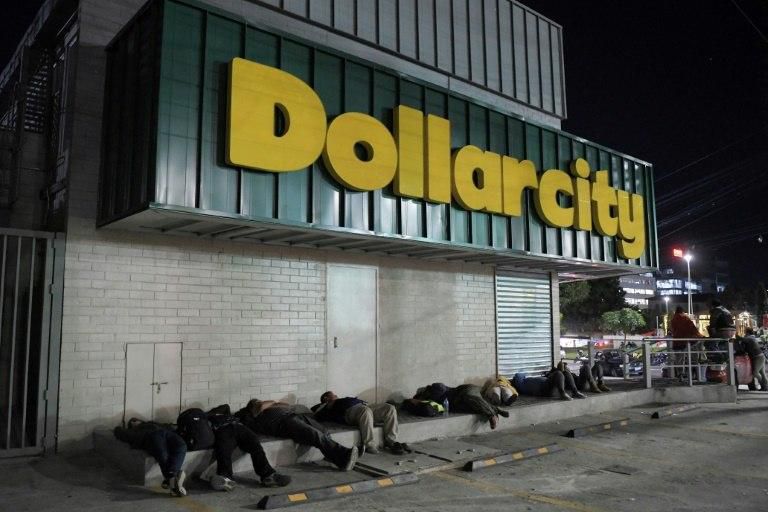 Salvadoran migrants huddled on the sidewalk in front of a shop called "Dollarcity" before a caravan departed