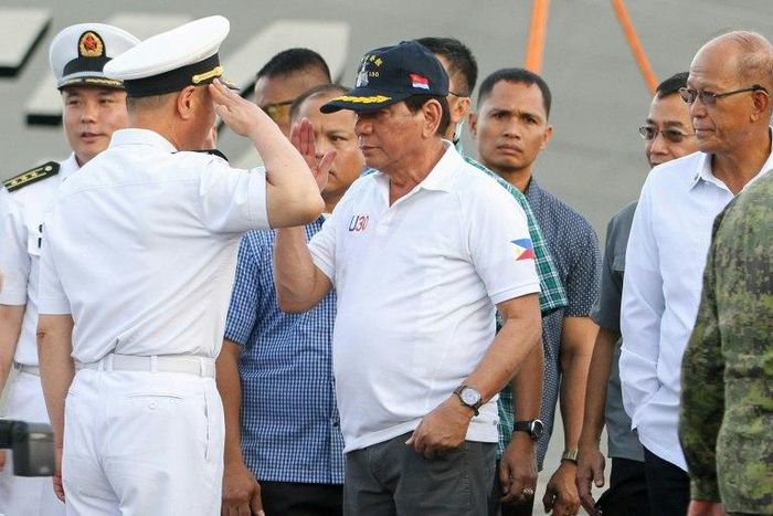 Philippine President Rodrigo Duterte (C) returns a salute from a Chinese naval officer as Philippine Defence Secretary Delfin Lorenzana (R) looks on during Duterte's visit to the Chinese warship Chang Chun in Davao on May 1, 2017