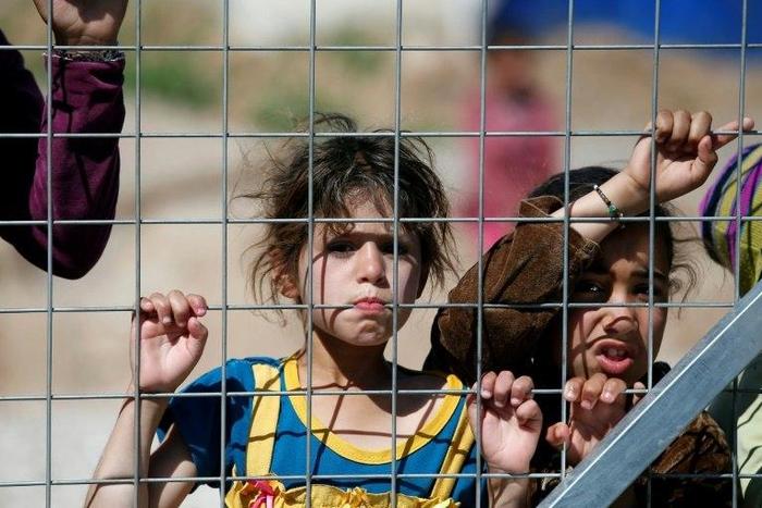 Iraqi children displaced from the battleground city of Mosul stand behind a fence at a camp in the village of Hasan Sham, 30 kilometres (18 miles) away