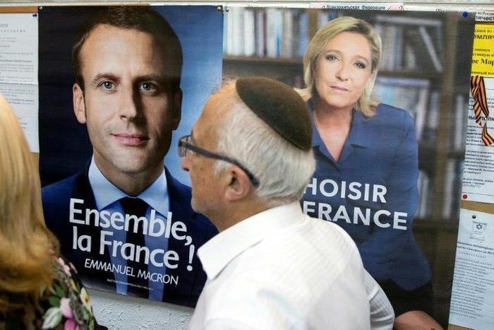 A French citizen walks past election posters of French presidential candidates Emmanuel Macron and Marine Le Pen before casting his vote at the French consulate in Tel Aviv on May 7, 2017