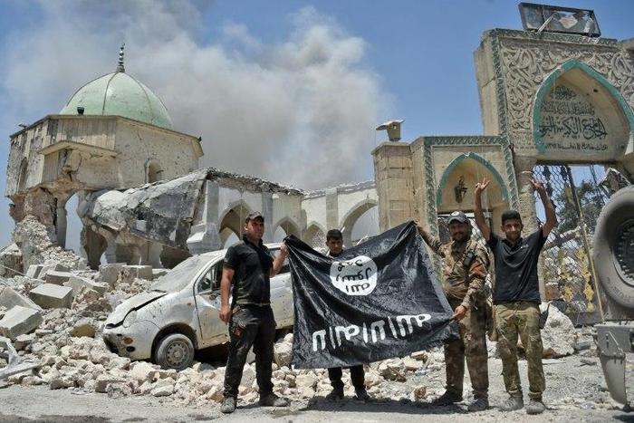 Iraqi soldiers pose with an upside-down flag of the Islamic State group outside the ruins of the Nuri mosque in the Old City of Mosul on June 30, 2017
