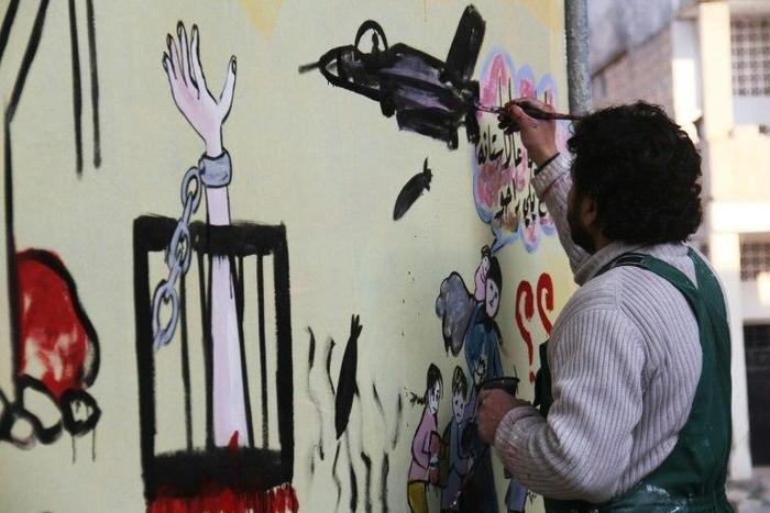 Syrian artist Aziz al-Asmar works on a mural depicting the war ahead of the start of the Astana peace talks, on January 19, 2017, in the rebel-held town of Binnish, Idlib province