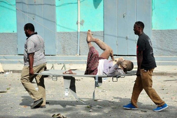 Residents carry an injured man wounded during a complex car bomb attack targeting a Mogadishu hotel on January 25, 2017